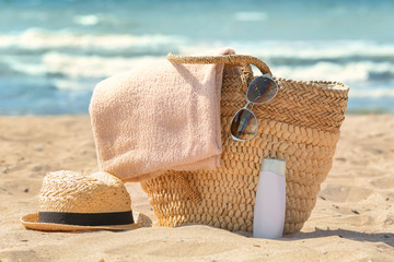 Bag with beach towel and summer accessories on sand