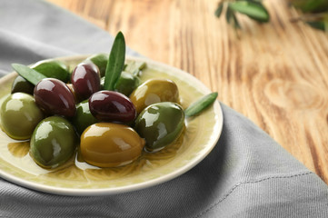 Plate with canned olives on wooden table