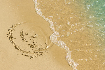 Children's drawing on a sandy sea beach. Smiling face drawn on yellow sand