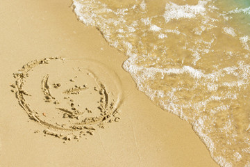 Children's drawing on a sandy sea beach. Smiling face drawn on yellow sand