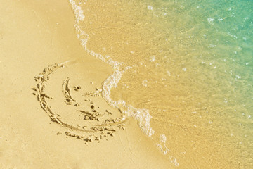 Children's drawing on a sandy sea beach. Smiling face drawn on yellow sand