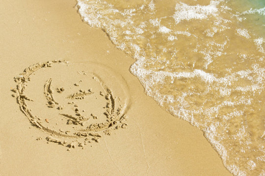 Children's drawing on a sandy sea beach. Smiling face drawn on yellow sand