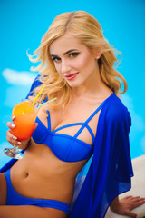 fashion outdoor photo of beautiful sensual woman wearing elegant bikini, posing beside swimming pool with cocktail