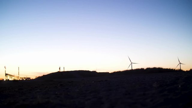 Dark silhouette of hills and windmills after sunset, with the city lighting the sky