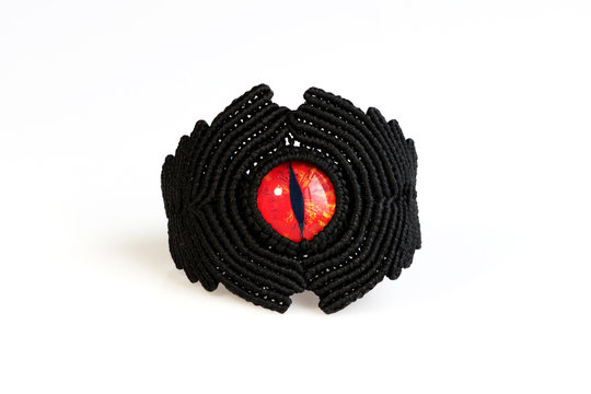 black bracelet for the hand from waxed thread, and red dragon eye in the technique of macrame on a white background.