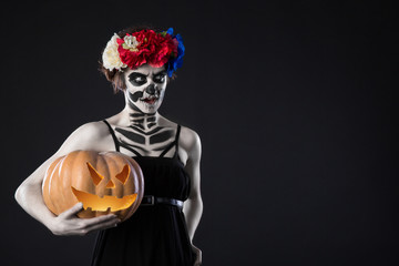 Portrait of woman with wreath and scary halloween makeup. Zombii in wreath with pumpkin over black background