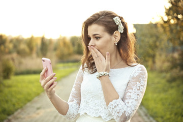 Shocked girl in wedding dress looking at mobile phone in pink cover