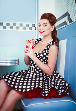 Retro (vintage) portrait of cheerful beautiful young girl sitting in cafe and drinking beverage. Pin up style portrait of young girl in dress