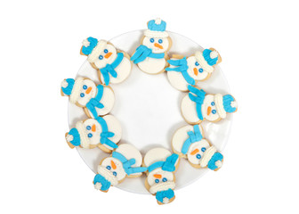 Snowman sugar cookies decorated with marshmallow fondant, blue royal icing scarf and hats arranged in a circle on a porcelain plate. Isolated on white background