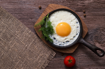 Fried eggs in a frying pan on a wooden background, top view.