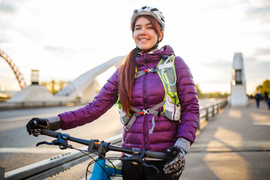 Photo of sportive woman in helmet on bicycle on bridge in city