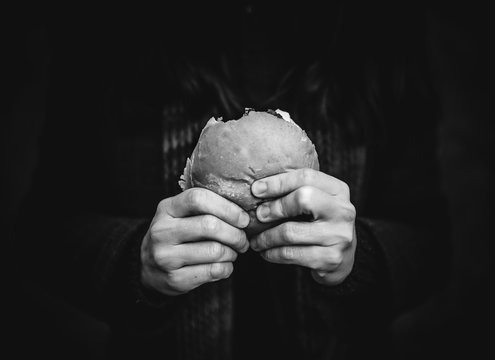 The concept of hunger and poverty. A roll or hamburger in the hands of a close up. Black and white monochrome photography.