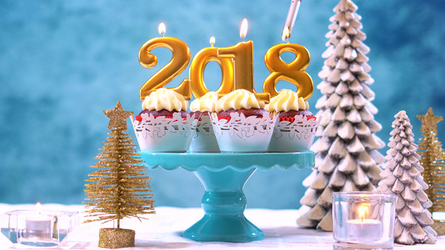 Happy New Year 2018 cupcakes on a modern stylish, festive, blue gold and white Winter theme table setting, close up with copy space lighting candles.