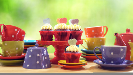 Colorful Mad Hatter style tea party with cupcakes and rainbow colored polka dot cups and saucers, with bokeh garden background and lens flare, with copy space.