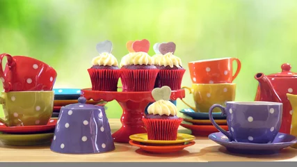  Colorful Mad Hatter style tea party with cupcakes and rainbow colored polka dot cups and saucers, with bokeh garden background and lens flare, with copy space. © millefloreimages