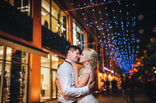 A pair of loving cut newlyweds gently embrace against the background of the evening city. Bokeh, the light of the lamps.