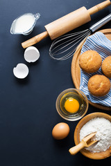 Baking ingredients. Bowl, eggs, flour, eggbeater, rolling pin and eggshells on black chalkboard from above.