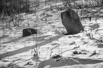 Black and white photograph of two headstones partially buried in snow and back lit with shadows.