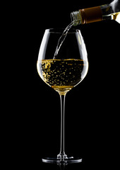 Pouring white wine from bottle to glass on black