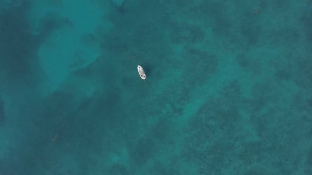 Drone looking straight down at a boat anchored in the middle of the Atlantic Ocean off the Florida Keys. The water is calm but enough to create an texture in the clear turquoise Caribbean sea. The sea