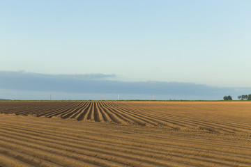 Plowed agricultural fields prepared for planting crops in Normandy, France. Countryside landscape with cloudy sky, farmlands in spring. Environment friendly farming and industrial agriculture concept.
