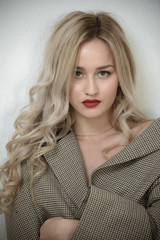 Blonde woman with long hair standing against white wall wearing check pattern short cabbardine