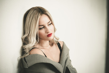 Blonde woman with long hair standing against white wall wearing check pattern short cabbardine