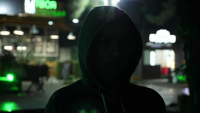 Silhouette of a man in a hood standing on a night street. 4k