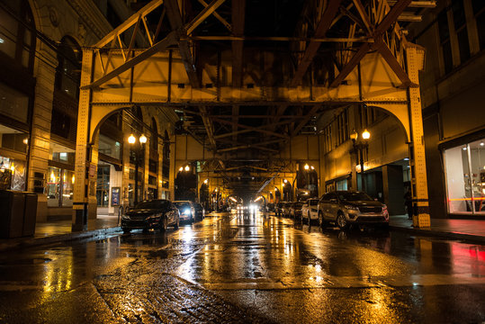 Night empty american city street with parked cars and subway in Chicago at rainy day