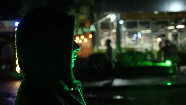 Silhouette of a man in a hood standing on a night street. 4k