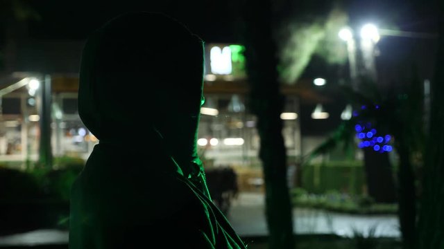Silhouette of a man in a hood standing on a night street. 4k