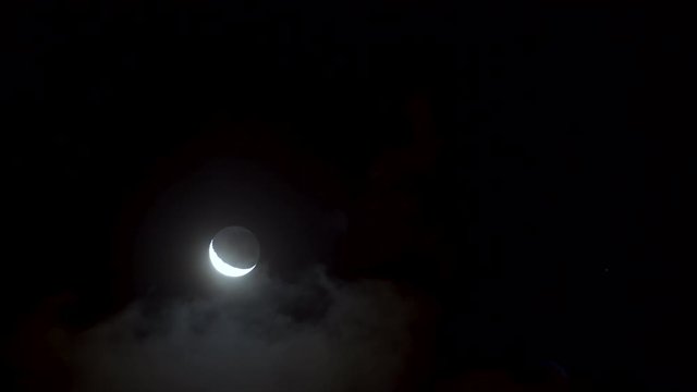 Young moon mooving through clouds at night