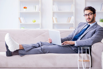 Businessman with crutches and broken leg at home working