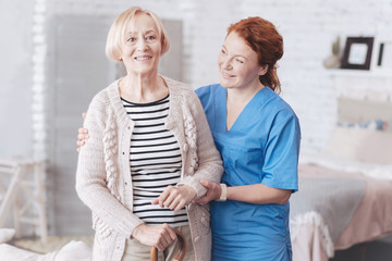 Cheerful caregiver helping her elderly patient to stand up