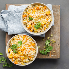 The perfect vegetarian dinner. Bulgur with pumpkin, carrots, spices (ginger, cinnamon, pepper, cardamom), honey and cilantro. A autumn gray concrete background for you.  Flat lay, top view