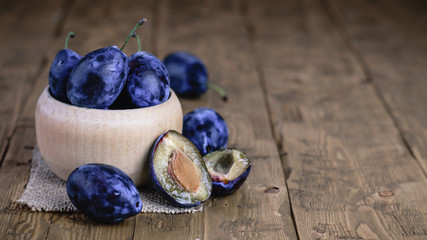 Sliced and whole plums in a bowl on a rustic table.