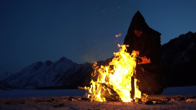 monk is warming around campfire in the winter mountains. 4K UHD
