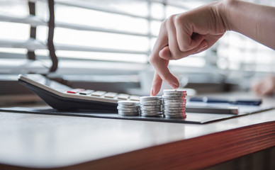 businesswomen use finger like a walk on the coin stack on the wooden table with calculator and graphic document.