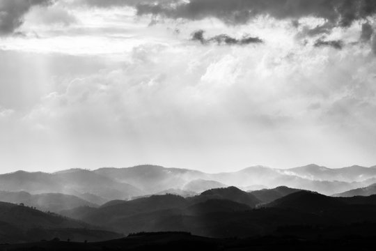 Various layers of hills and mountains with mist between them, with sun rays coming out through the clouds © Massimo