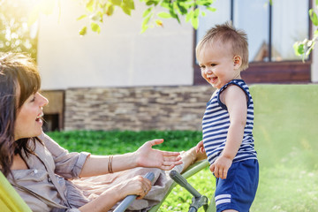 funny little boy one year with his mother, outdoor portrait. On the lawn next to the house, happiness, fun, family, rest