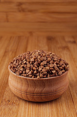 Buckwheat brown in wooden bowl on brown bamboo board, closeup.