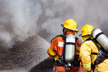two firefighters water spray by high pressure nozzle to fire surround with smoke and copy space