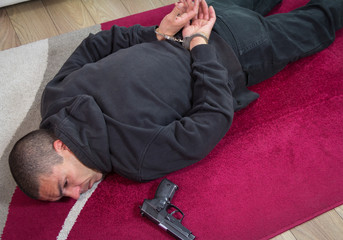 The burglar lies on the floor with handcuffs facing back to the floor. A gun next to him found during the search