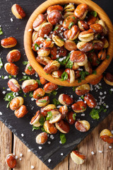 fried broad beans with salt and herbs in a bowl close-up. Vertical top view