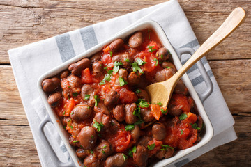 Vegetarian food: spicy beans with tomatoes and greens close-up. Horizontal top view