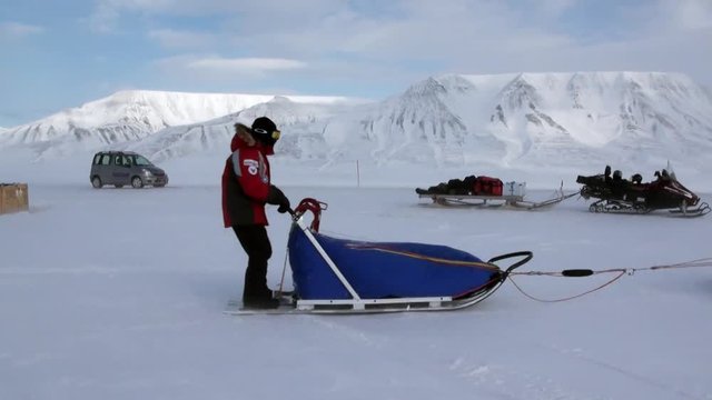 People expedition on dog sled team husky Eskimo road of North Pole in Arctic. Way from airport Longyear to Pyramid Spitsbergen on background of glacier mountains Svalbard in Norway.