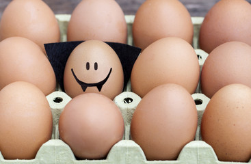 Smiling egg  dressed up as a vampire wearing souronded by blank brown eggs.
