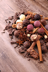 A selection of assorted chocolate truffle pralines on a wooden table with dark chocolate, cinnamon and anise.
