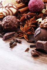 A selection of assorted chocolate truffle pralines on a wooden table with dark chocolate, cinnamon and anise.