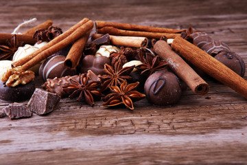 A selection of assorted chocolate truffle pralines on a wooden table with dark chocolate, cinnamon and anise.